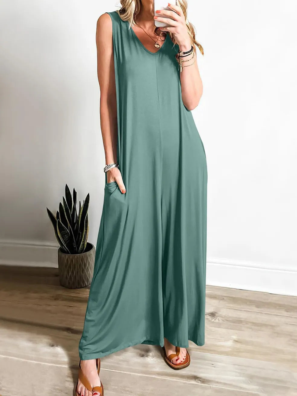 Teal V-neck jumpsuit with wide legs, modeled indoors with a plant in the corner.