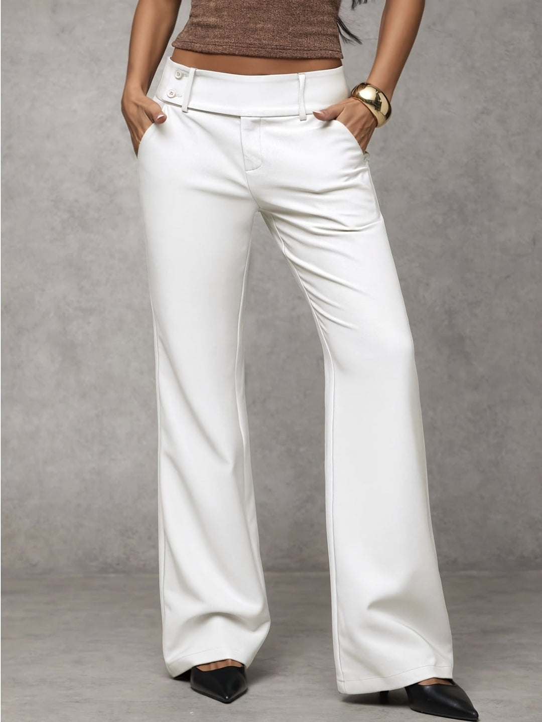 White modern pants with button detail, modeled with hands in pockets. Indoor gray background.