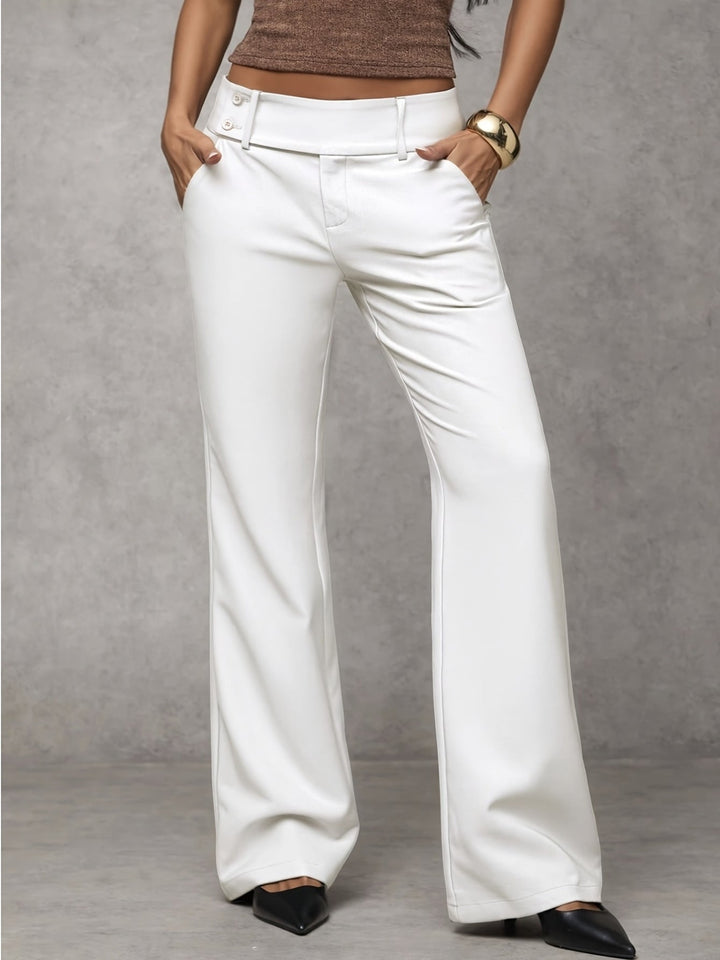White modern pants with button detail, modeled with hands in pockets. Indoor gray background.