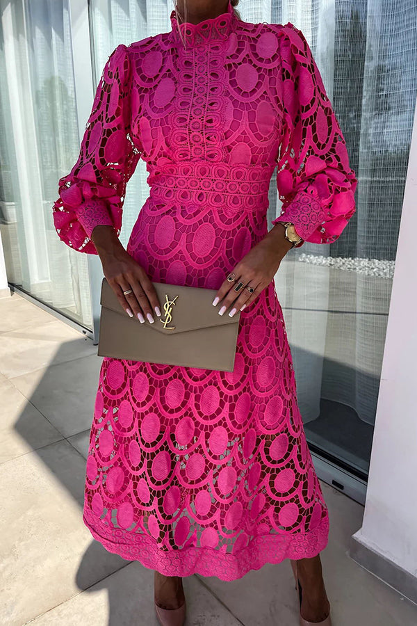 Bright pink lace dress with detailed patterns, long sleeves, high neckline, holding a beige clutch. Studio setting with glass window.