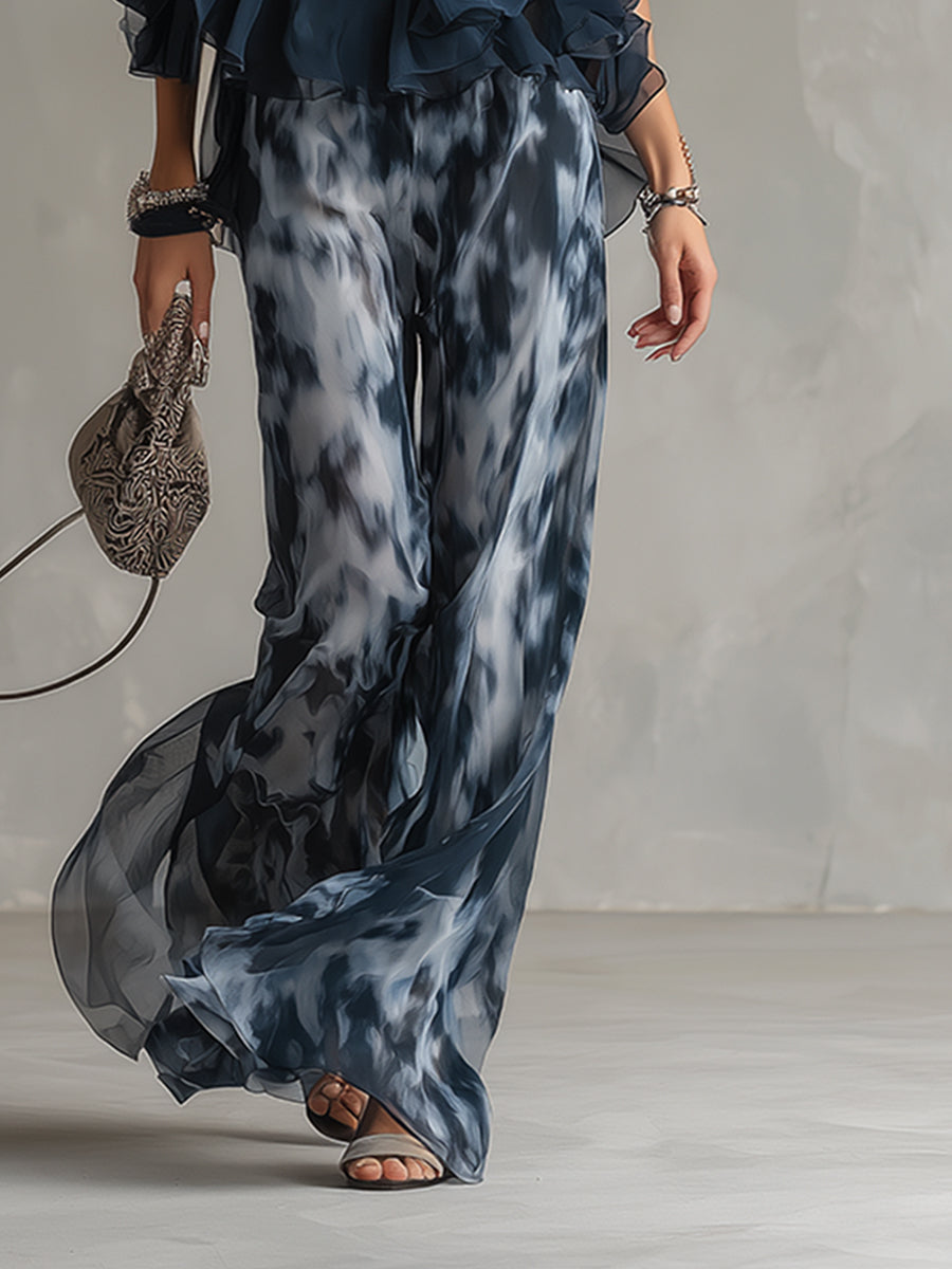 Close-up of wide-leg patterned pants and sandals, holding a delicate handbag. Studio setting.
