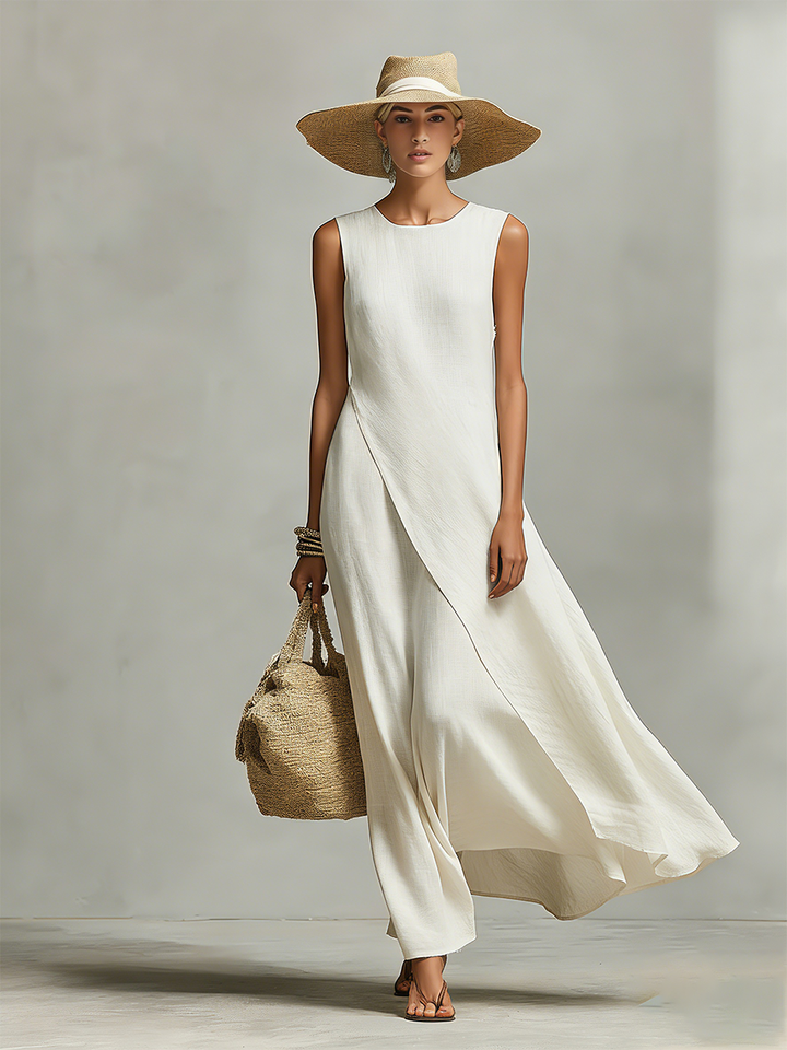 Front view of a woman in an ivory loose-fit maxi dress, wearing a wide-brimmed hat, holding a woven bag, studio backdrop.