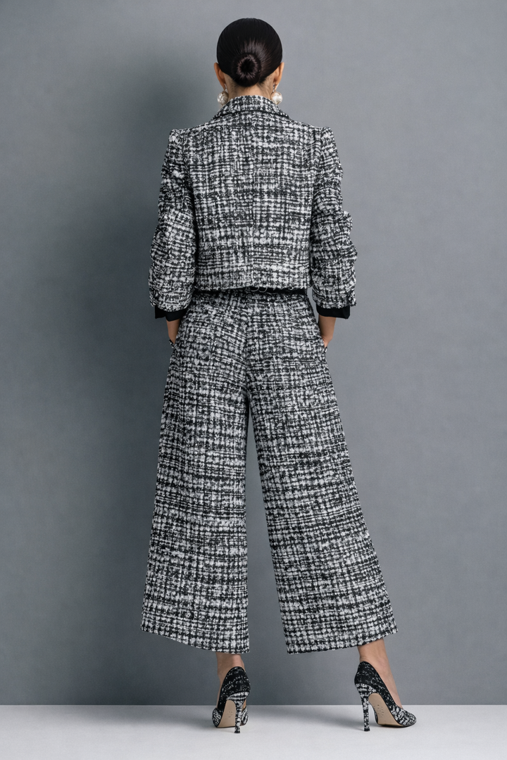 Back view of a woman in a black and white patterned pantsuit, hands in pockets, gray studio setting.