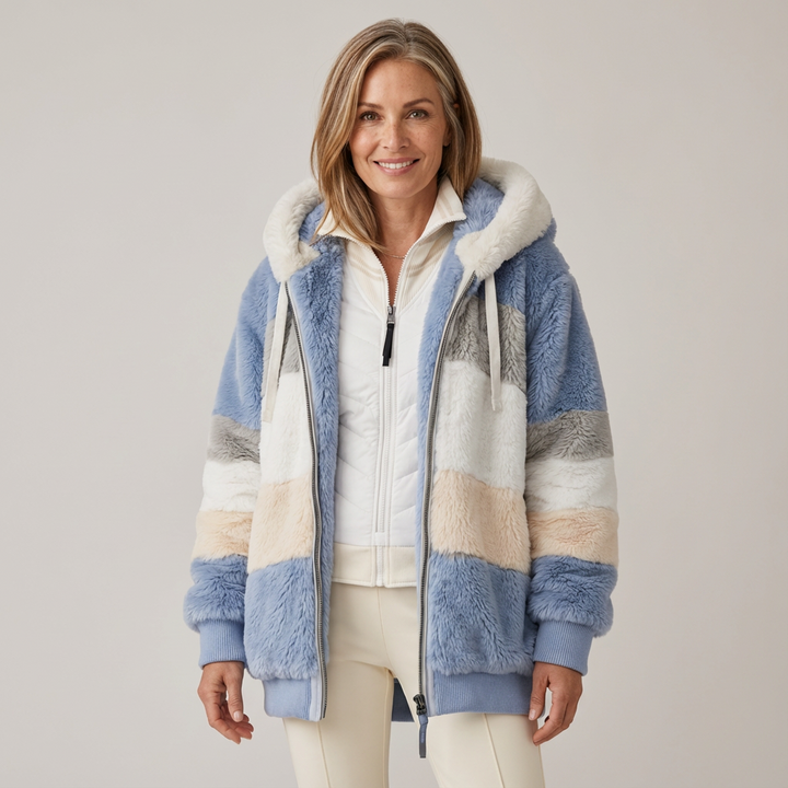 Woman wearing a plush, multicolored hooded jacket in white, blue, and beige stripes, in a studio setting.