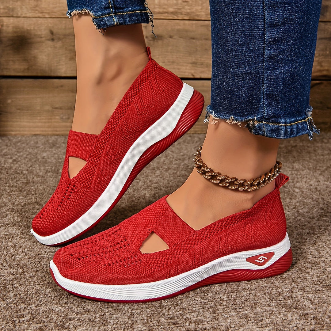 Red non-slip orthopedic shoes worn with anklet, denim jeans on carpeted floor.