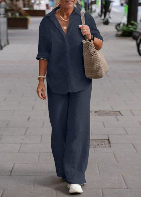 Woman wearing a deep blue two-piece set with rolled sleeves, walking with a beige woven bag in an urban area.
