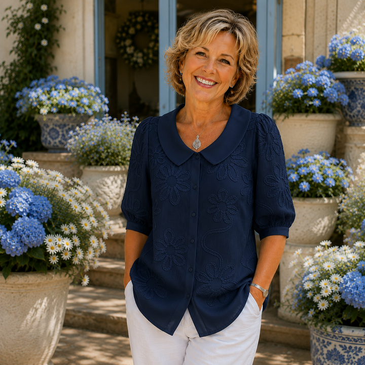 Woman in a navy floral blouse poses in garden setting with blue and white flowers.