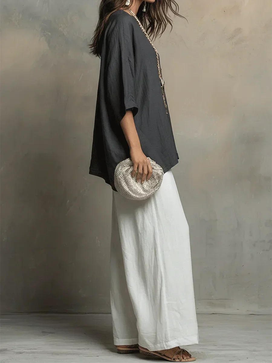 Side view of woman in dark top and white pants, holding textured clutch, studio backdrop.