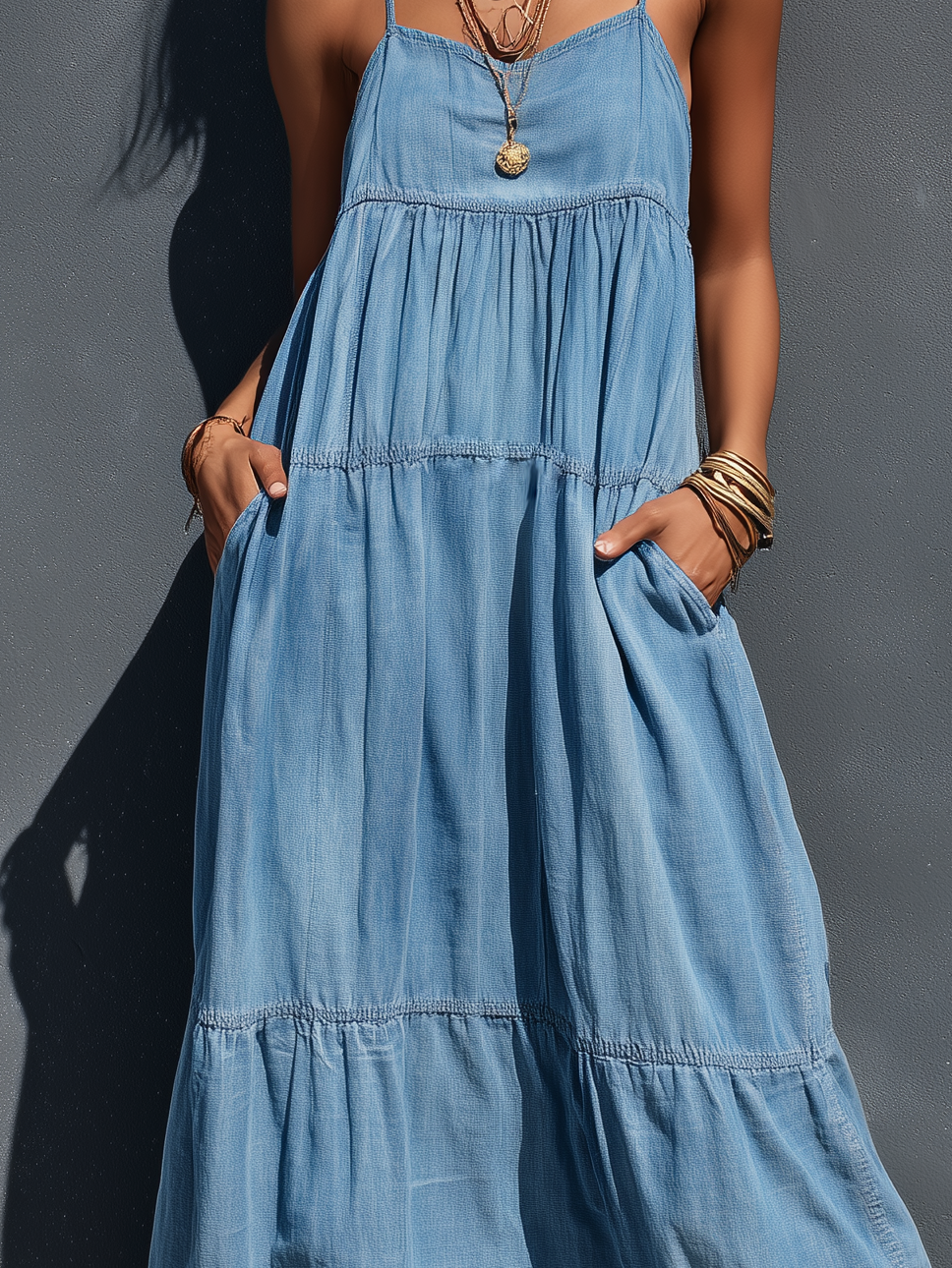 Close-up of blue suspender maxi dress details, highlighting the fabric texture and pockets, with a gray background.