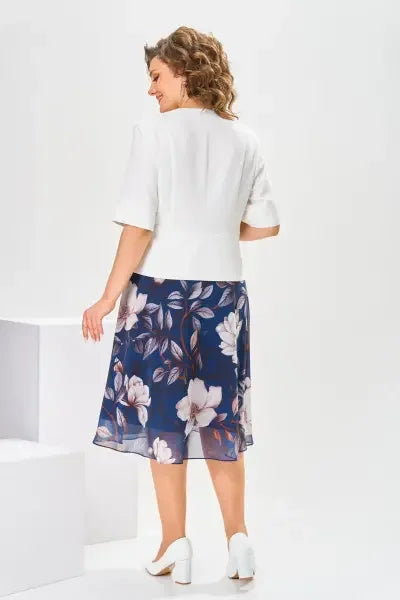 Rear view of woman in a white top and navy floral midi skirt, against a white studio backdrop.