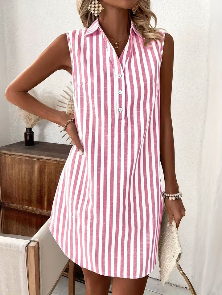 Pink striped shirt dress with button detail, accessorized with earrings and bangles, against a white wall with wooden furniture.