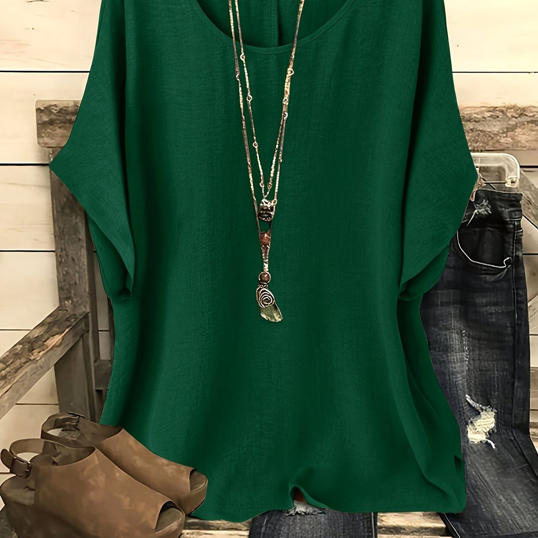Forest green loose summer top on hanger with necklace, sandals, and jeans on rustic bench.