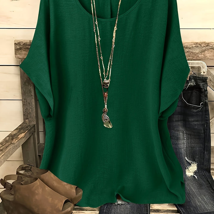 Forest green loose summer top on hanger with necklace, sandals, and jeans on rustic bench.
