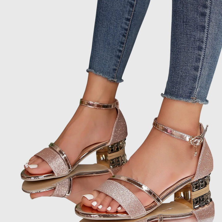 Orthopedic pink glitter heeled sandals with gold accents, worn with frayed hem jeans, on a reflective surface.