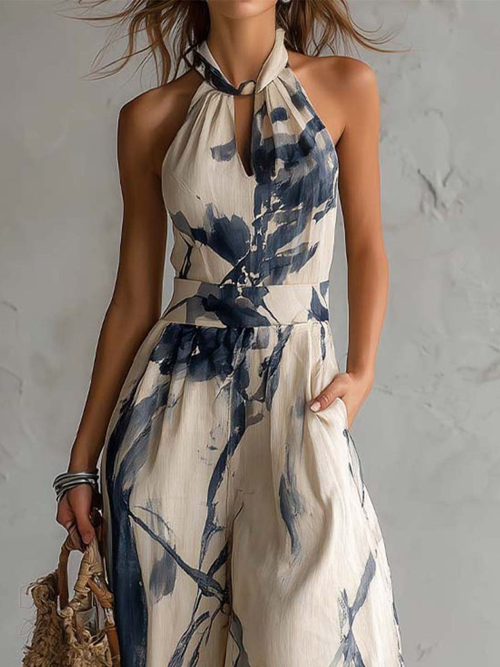 Close-up of halter-neck jumpsuit top, blue abstract on beige, worn by woman in studio. Textured wall background.