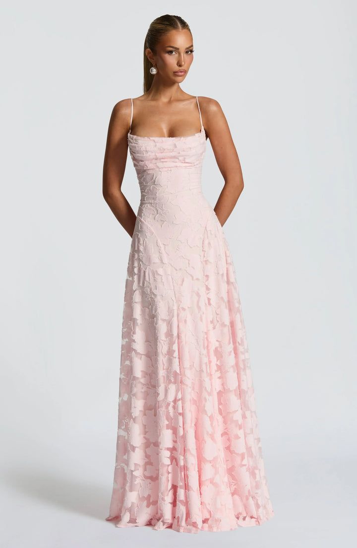 Elegant maxi dress in light pink with floral texture, thin straps, and floor-length design in a studio setting.