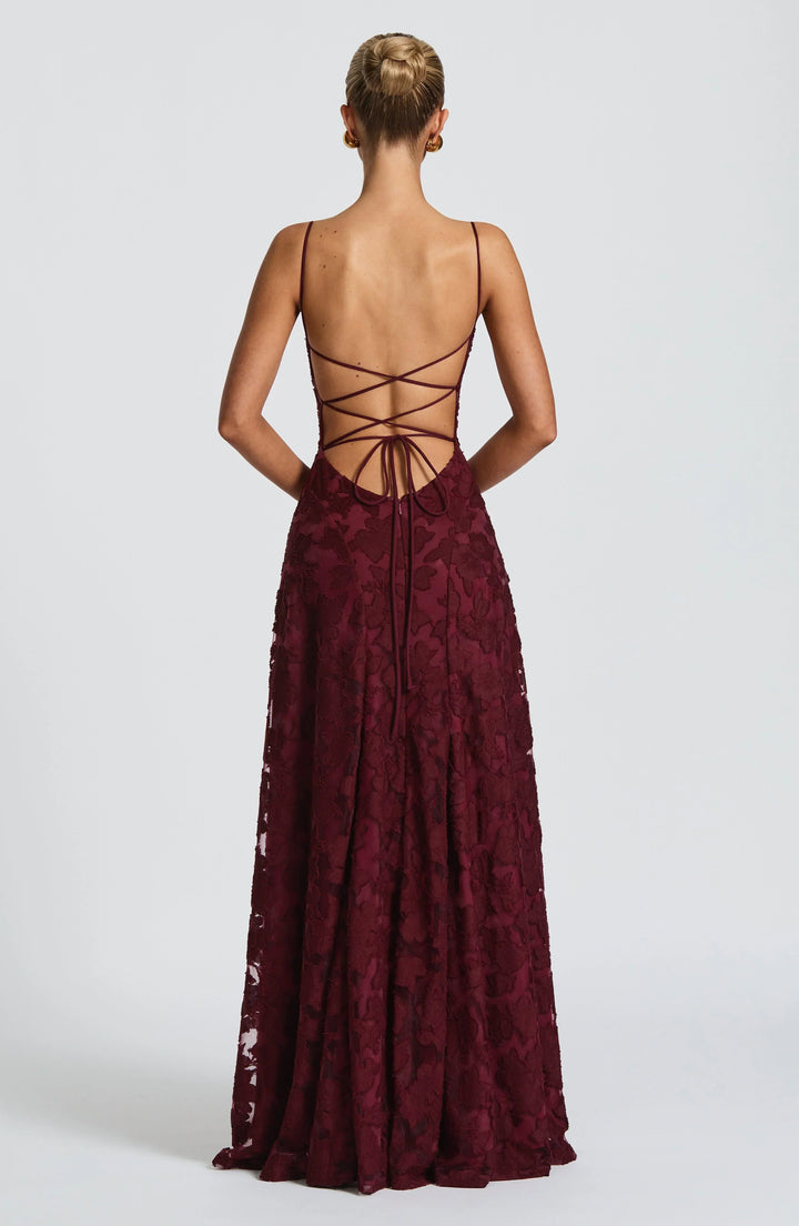 Back view of deep red maxi dress with criss-cross strap detailing in a studio setting.