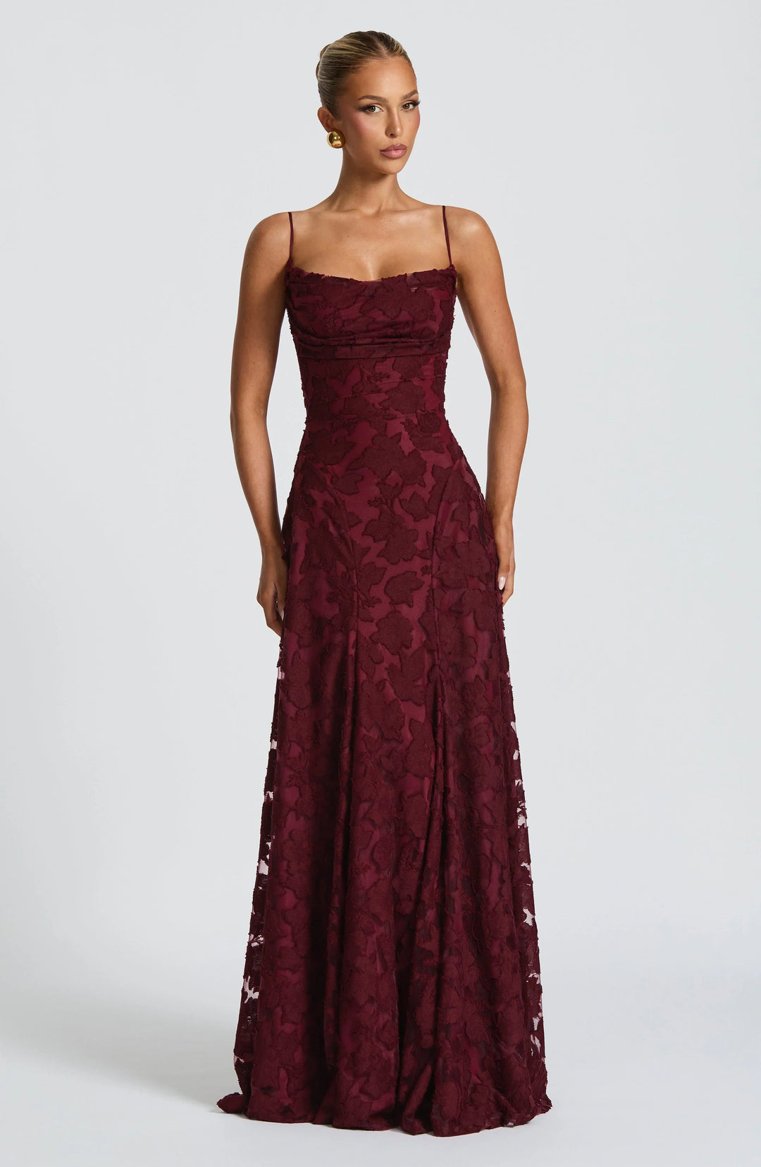 Elegant maxi dress in deep red with floral texture, thin straps, and floor-length design in a studio setting.
