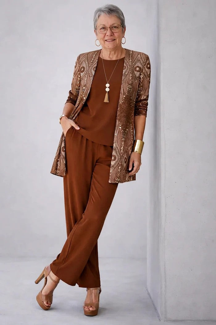 Woman in a stylish brown three-piece outfit with a decorated cardigan. Light grey studio setting.
