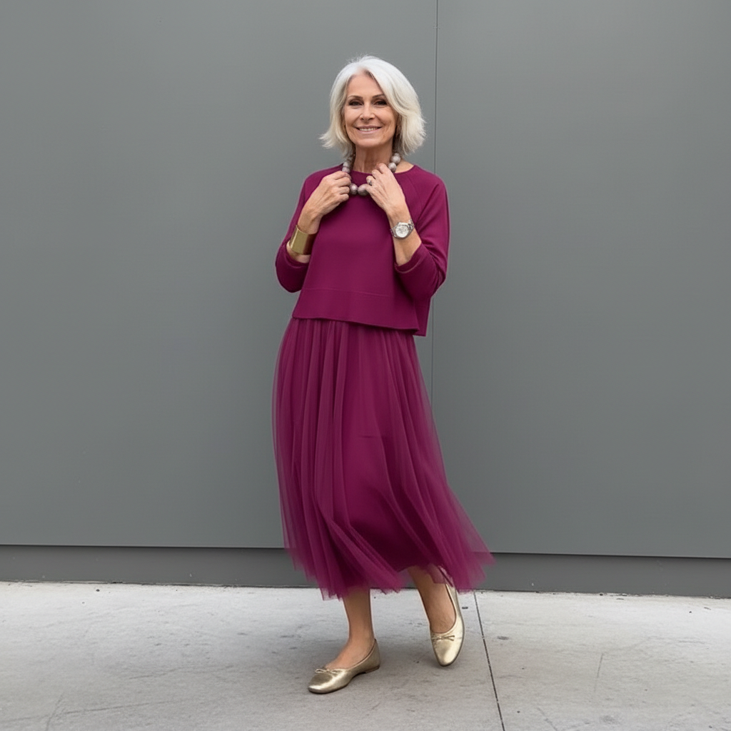Woman in burgundy pleated skirt outfit with beaded necklace, outdoor setting.