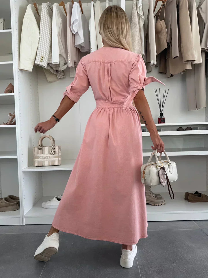 Back view of pink denim dress with tied sleeves, worn by a person holding a white bag, in a closet setting.
