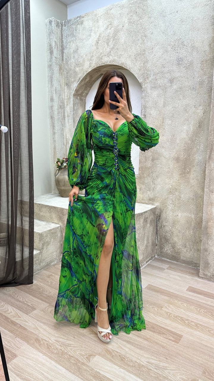 Green off-shoulder dress with ruched front and floral detailing, worn indoors against a textured wall with sheer curtains.