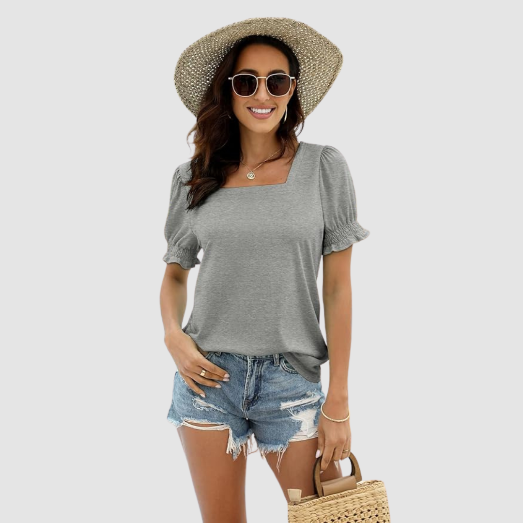Woman in gray square neck top, ripped denim shorts, straw hat, sunglasses, holds woven bag, neutral backdrop.