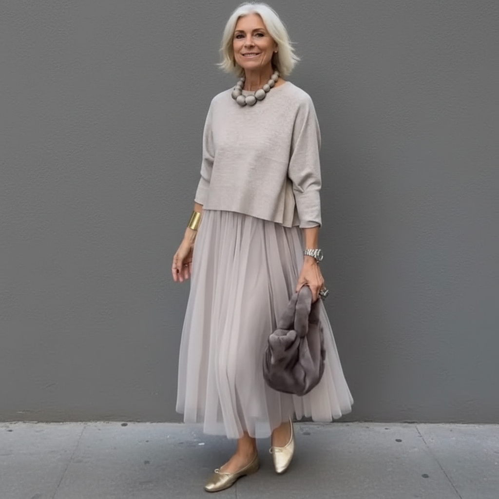 Sophisticated woman in gray pleated skirt outfit, with a plush bag, standing in an urban area.