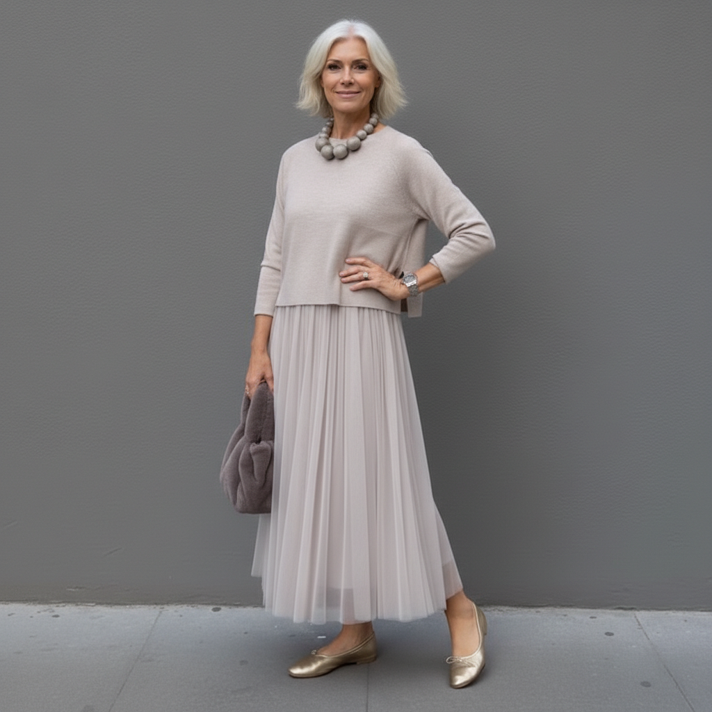Sophisticated woman in gray two-piece outfit with pleated skirt, accessorized with a plush bag, outdoor setting.