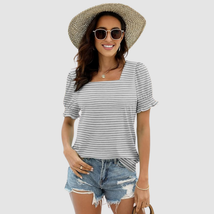 Model in gray-striped top, denim shorts, straw hat. Casual look in studio setting.