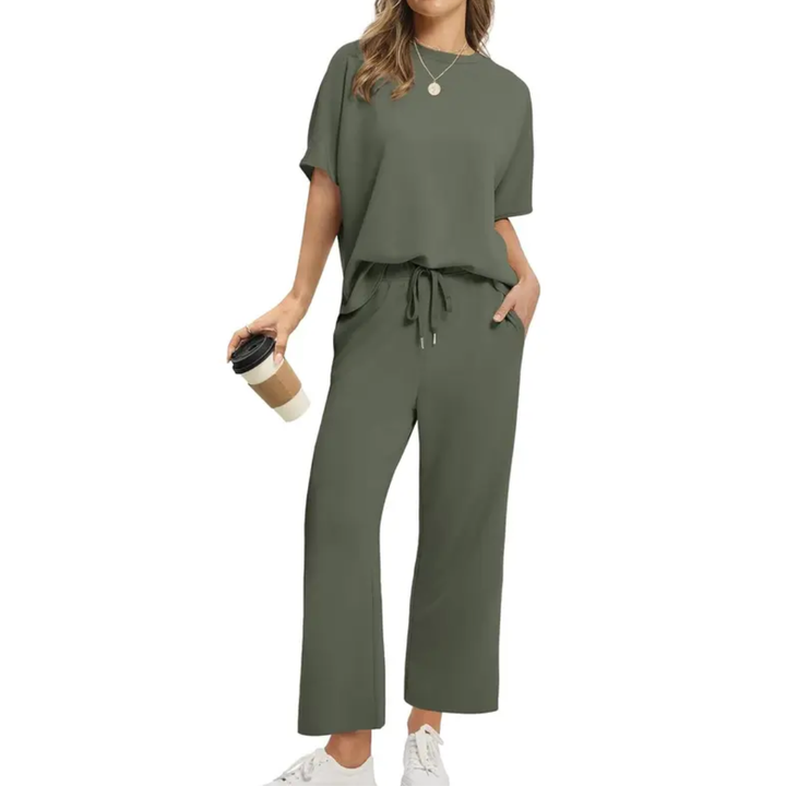 Woman showcasing a trendy olive set with loose top and drawstring pants, holding a coffee, studio background.