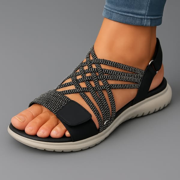 Black orthopedic comfort sandal with crisscross straps on foot, displayed on gray background.