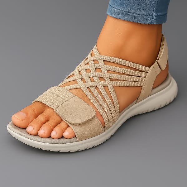 Beige orthopedic comfort sandal with crisscross straps on foot, displayed on gray background.