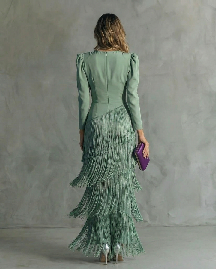 Back view of a sage green dress with layered fringe on a woman, holding a purple clutch, in a gray minimalist room.