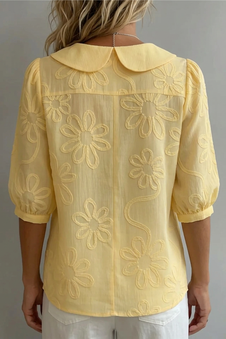 Back view of yellow floral blouse on a woman, neutral background.