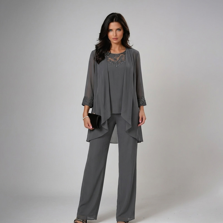 Model in elegant gray three-piece set with lace accents, holding a black clutch in a studio.