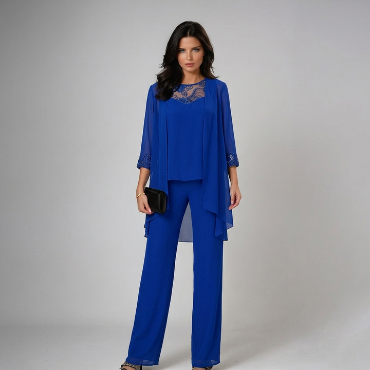 Model in vibrant blue three-piece set with lace accents, holding a black clutch in a studio setting.