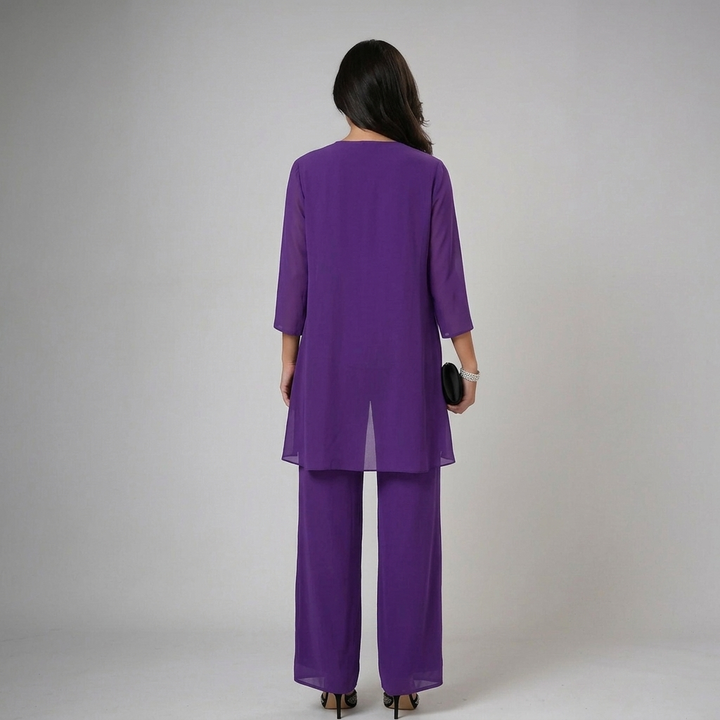 Back view of model in purple set with lace cuffs, holding a clutch in a studio backdrop.