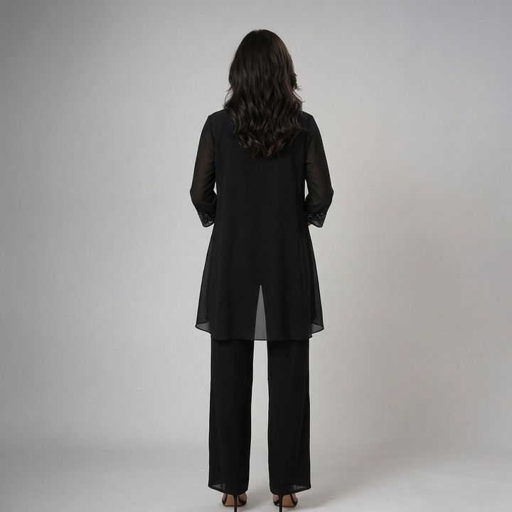 Back view of model in black set with lace cuffs, holding clutch in a studio environment.