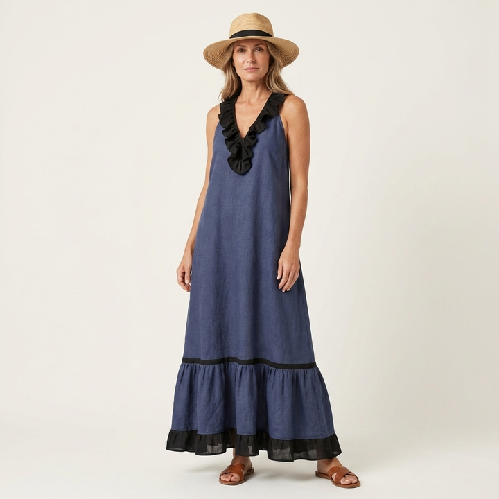 Woman in dark blue sleeveless maxi dress with ruffle-neck and contrast trim, wearing hat, in studio.