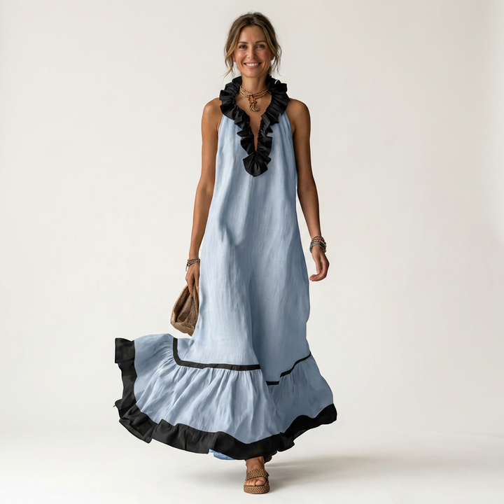 Woman in light blue sleeveless maxi dress with ruffle-neck and contrast trim, walking with bag in studio.