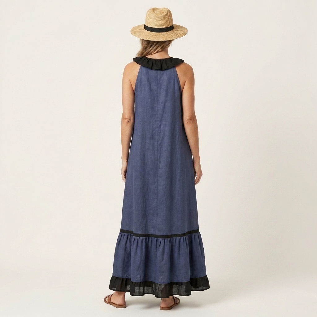 Back view of woman in dark blue sleeveless maxi dress with ruffle-neck and contrast trim, wearing hat in studio.
