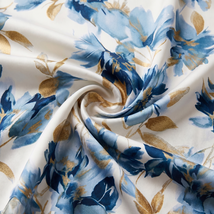 Close-up of a floral fabric featuring blue and gold flowers twisted to show texture in a studio setting.