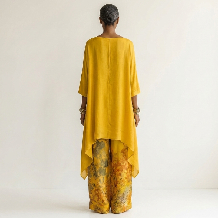 Back view of model in yellow flowing set with floral pants, against a light studio backdrop.