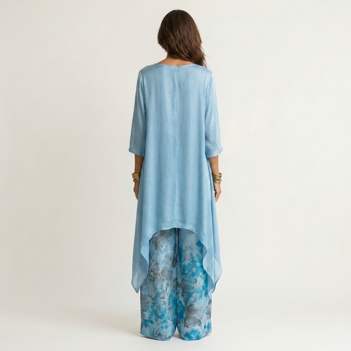 Back view of light blue elegant set with flowing top and floral wide-leg pants in studio.