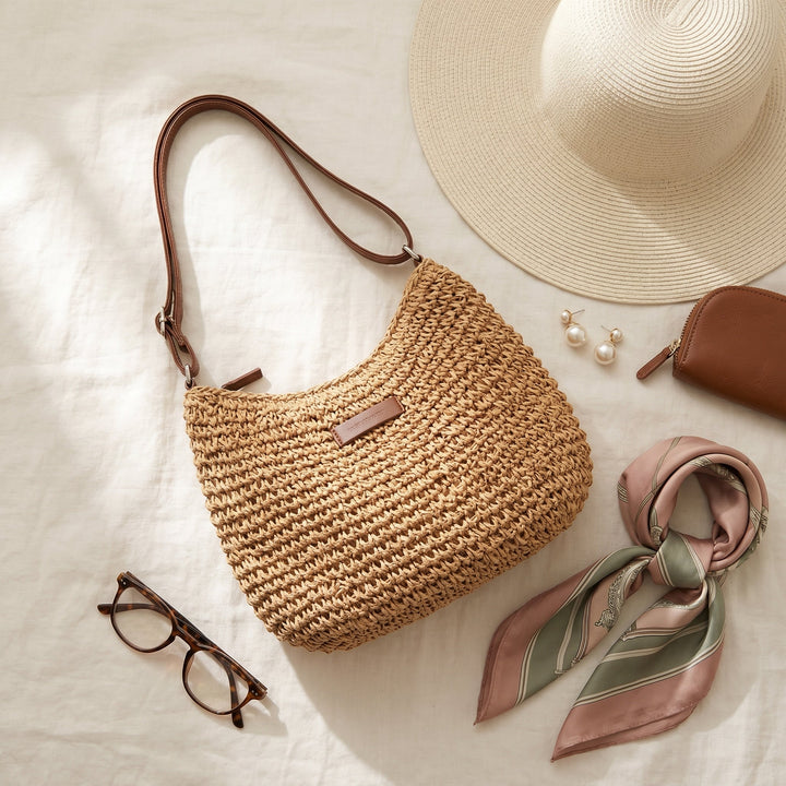 Woven bag with accessories, including a sun hat and scarf, on a light surface.