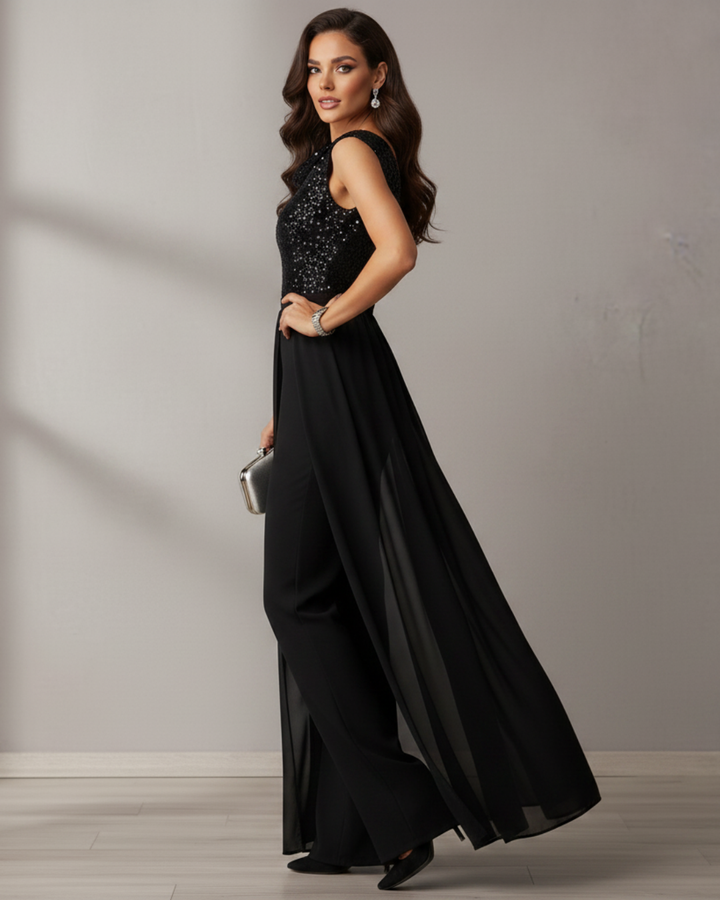 Side view of black jumpsuit with sequins and sheer overlay, woman holding silver clutch, studio setting.