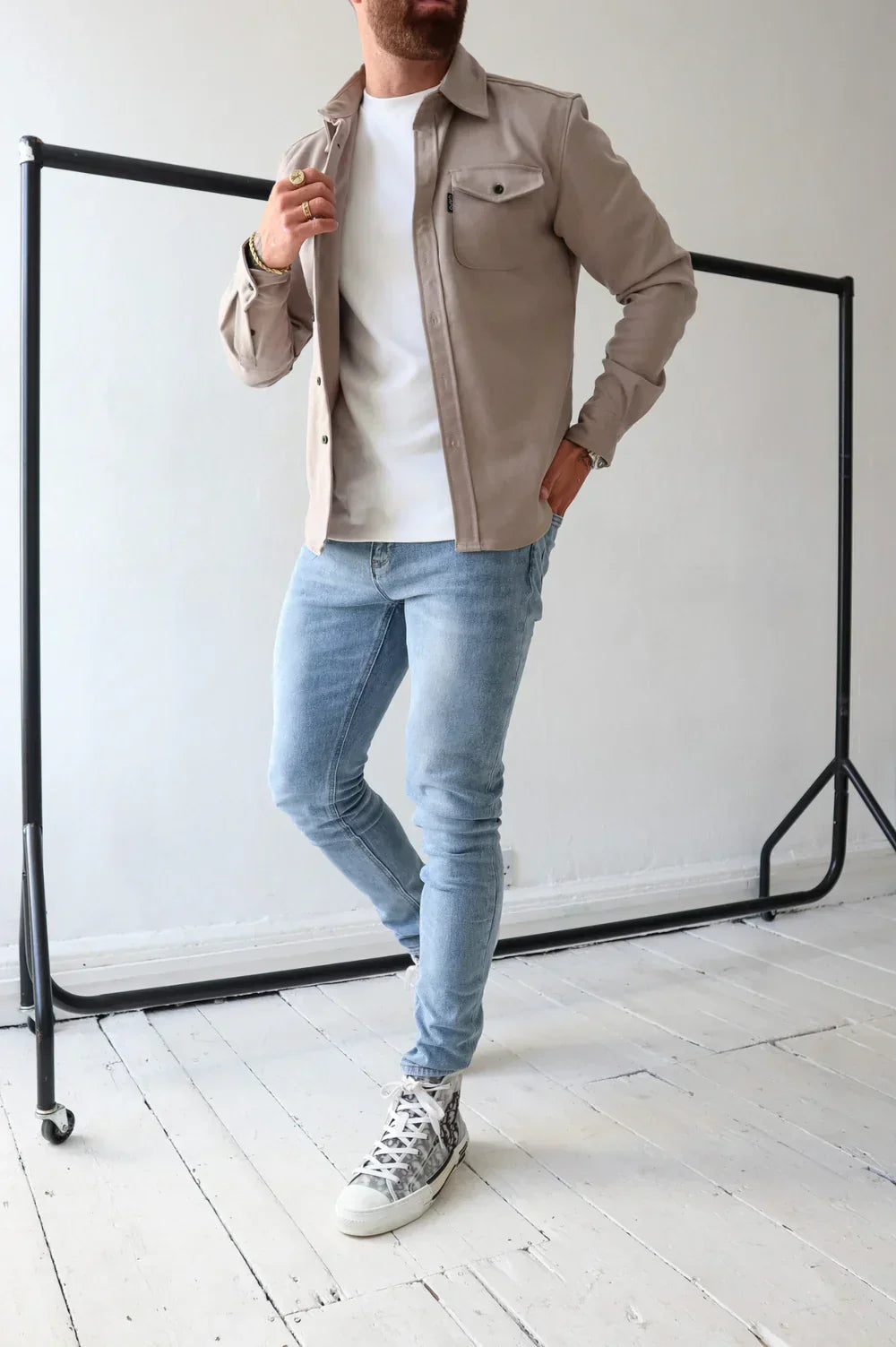 Taupe overshirt over white t-shirt and light jeans, standing indoors beside rail.