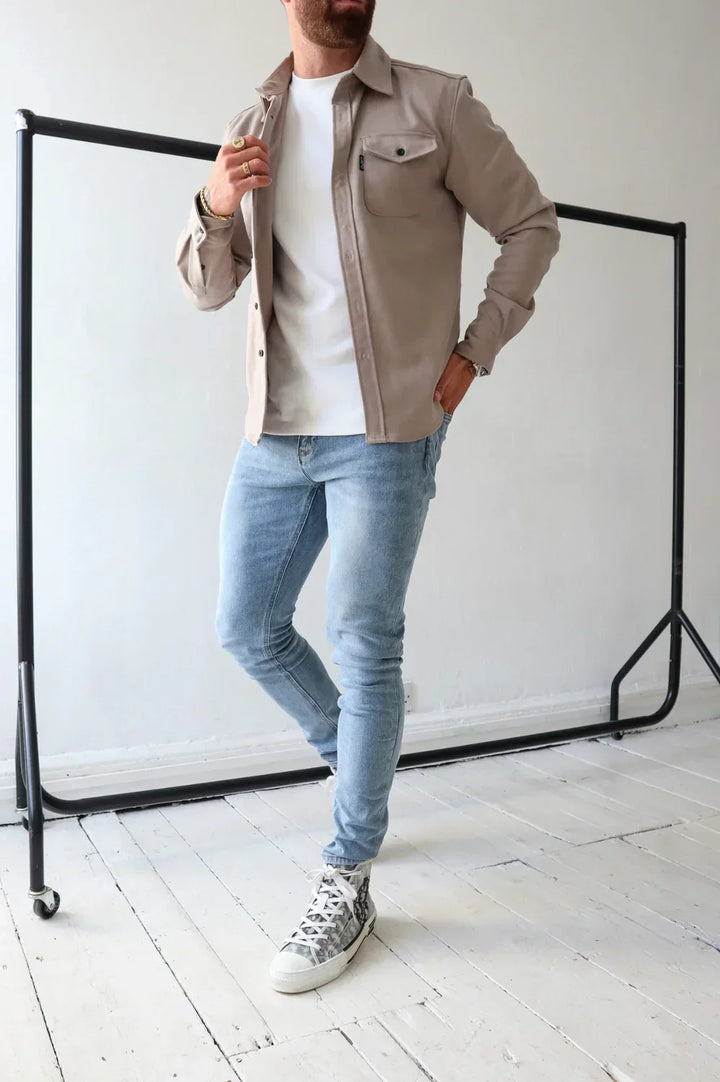 Taupe overshirt over white t-shirt and light jeans, standing indoors beside rail.