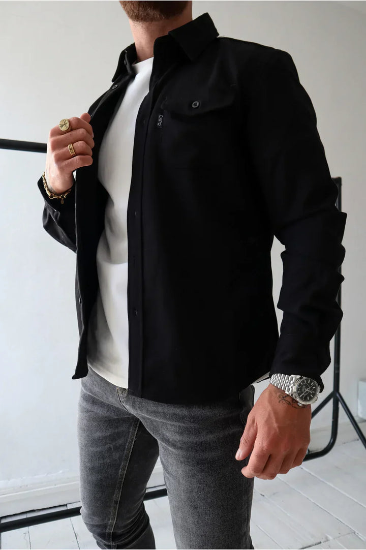 Black overshirt over white t-shirt and jeans, person adjusting cuffs, indoors.